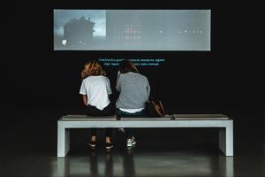 A person sitting on a bench in front of a television reading video subtitles