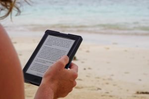 A person sitting at a beach reading content on a tablet