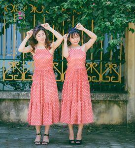 Twin girls in red dresses standing in front of a flower