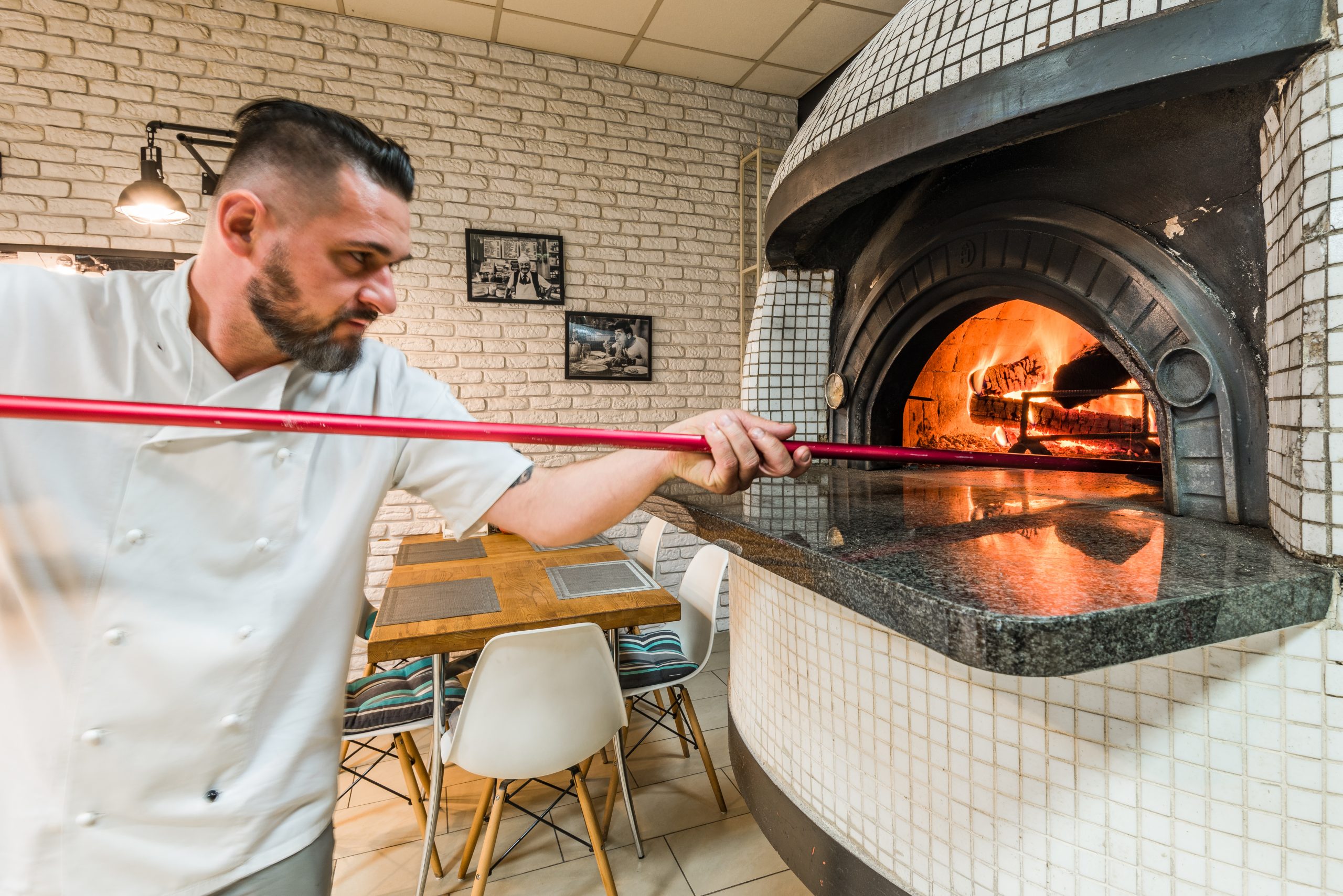 Handsome pizzaiolo man baking pizza in woodfired oven in local pizzeria